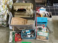 Overall lot showing sewing machine in case with accessory boxes, scissors, manuals and notions