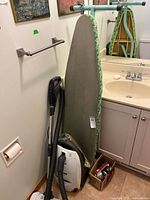 Vacuum cleaner, ironing board and box with iron grouped in bathroom