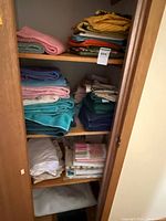 Closet shelves with stacks of towels, sheets, pillowcases, placemats
