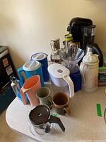 Countertop view showing Nespresso coffee maker, milk frother, pitchers, mugs, dripper, carafe, thermal carafe and bottle