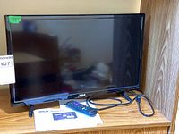 Front view of RCA 23-inch Roku TV on shelf with remote, power cord, manual visible