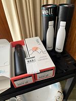 Two boxed LARQ bottles (one opened showing matte black bottle) and two S'well bottles in cylindrical packages