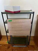 Shelving unit with TV tray leaning against front and box of legs on top