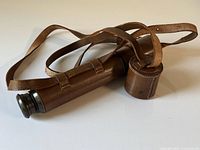 Telescope collapsed inside leather covering with attached shoulder strap and lens cap