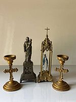 Group shot of two gilt cross candle holders and two metal saint statues