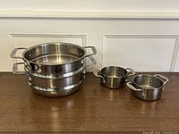 Group shot of four All-Clad stainless steel cookware pieces: two stacked steamer pots and two small saucepans