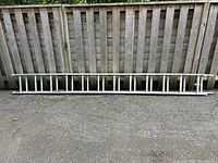 Full view of ladder in collapsed state leaning on fence