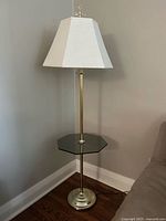 Full view of brass floor lamp with glass table and shade