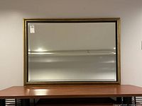 Front view of rectangular gold and black framed mirror on table