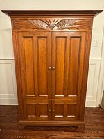 Front view of solid wood armoire showing carved crown and paneled doors