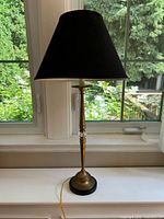 Full view of brass and glass table lamp with black shade on windowsill