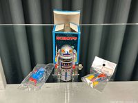 Set of 3 vintage tin toys including a tin robot toy with original box, a rocket ship toy, and a small sealed tin toy.