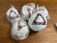 Five white Spalding soccer balls with maroon and blue designs, each sealed in clear plastic packaging, displayed on a wooden floor.