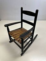 Full view of the vintage child's wooden rocking chair showing slat seat and black paint with eagle stamp on backrest.