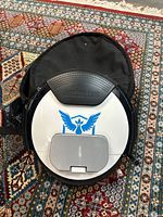Top view of white Ninebot One electric unicycle showing blue bird emblem and black protective cover, positioned on patterned carpet.