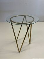 Side angle view of the round glass top table and gold-colored metal base with three angled legs.