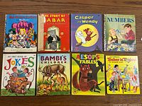 Photo of 8 children's books arranged in two rows with colorful covers and titles visible.