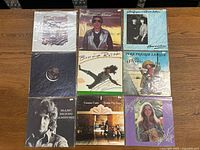 Group of 9 various LP records arranged on wooden surface with album cover art visible showing Bonnie Raitt, Pure Prairie League and others.