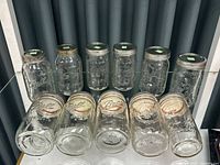 Top view showing 11 tall glass canning jars with metal lids, some lids rusty