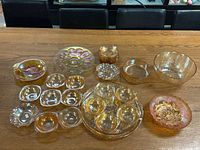 Overall display of multiple marigold carnival glass items with varied shapes including bowls and divided dishes on wooden table