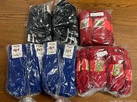 Seven pairs of multisport socks in blue, red, and black, sealed in plastic packaging, displayed on a wooden floor.