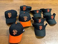 Eight San Francisco Giants caps and visors arranged on a wooden surface showing color, logo, and styles.