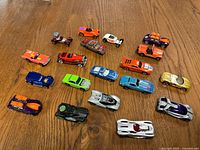 Top-down view of all 18 assorted toy cars on a wooden floor, showing various colors, shapes and paint details.