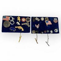 Two blue velvet pads with assorted vintage metal tie tacks in patriotic and police themes, including guns, flags, badges, and animals.