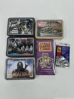 Photo showing five metal tins with Star Wars themes including Mandalorian and a box of The Great Dalmuti collector cards plus a sealed 1992 collector cards pack.