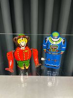 Front view of both vintage tin toys: a robot and a monkey in a suit with moving arms.