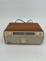 Front view showing wood finish, speaker grille, tuning and volume knobs, and brand name.