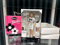 Barbie doll in original See's Candies themed packaging beside the branded shopping bag.