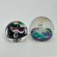 Two glass paperweights side by side showing colorful bubble designs inside clear glass domes.