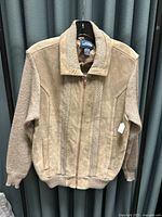 Front view of the vintage Mervyn's men's knit and suede jacket hanging on a hanger against a dark backdrop