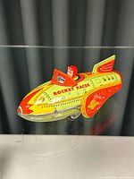 Front and side view of the vintage rocket racer tin toy highlighting its colors, the pilot figure, and printed text.