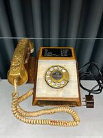 Photo of vintage rotary phone showing entire handset, rotary dial with personalized number, wood base, and coiled cord with plug