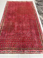 Photo showing full view of the red Persian rug with an all-over small patterned design and border on light tiled floor.