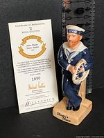 Front view of figurine beside certificate, ruler for scale