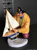 Front view of figurine showing sailor with sailboat and ruler for scale