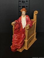 Front angled view of seated regal lady figurine highlighting pose, gown color and chair design