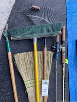 Group view of both fishing rods, reel, rake, weeder, push broom and straw broom on ground