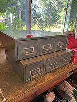 Both grey metal 3-drawer cabinets stacked on workbench