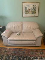 Front view of beige leather love seat with care kit on seat