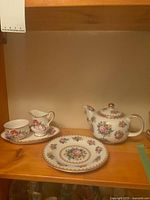 Group view of teapot, plate, creamer, sugar bowl and tray on shelf