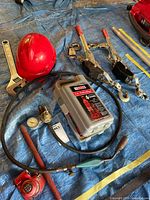 overview of lot on blue tarp showing hard hat, wrench, hose with torch, 4-ton jack in case, 2-ton jack and pullers