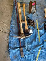 Overview of pickaxe, sledgehammer, axe, pry bar, chain, and wire spool on tarp
