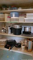Shelf with multiple cookware pieces including aluminum and enamel pots, roasting pans, percolator
