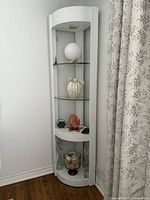 Full view of white corner display shelf showing curved front, two glass shelves, bottom shelf, top light housing