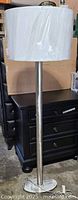 Full view of brushed metal floor lamp with white drum shade