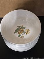 Stack of eleven white bowls with yellow daisy design visible on top bowl